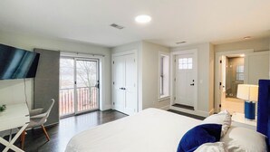 A hotel room with a large bed, a desk, and a chair. There is a door leading to a bathroom and a balcony. - 6-bed, Close to City, Roof deck! Private Bathroom per Bedroom! (Boston)
