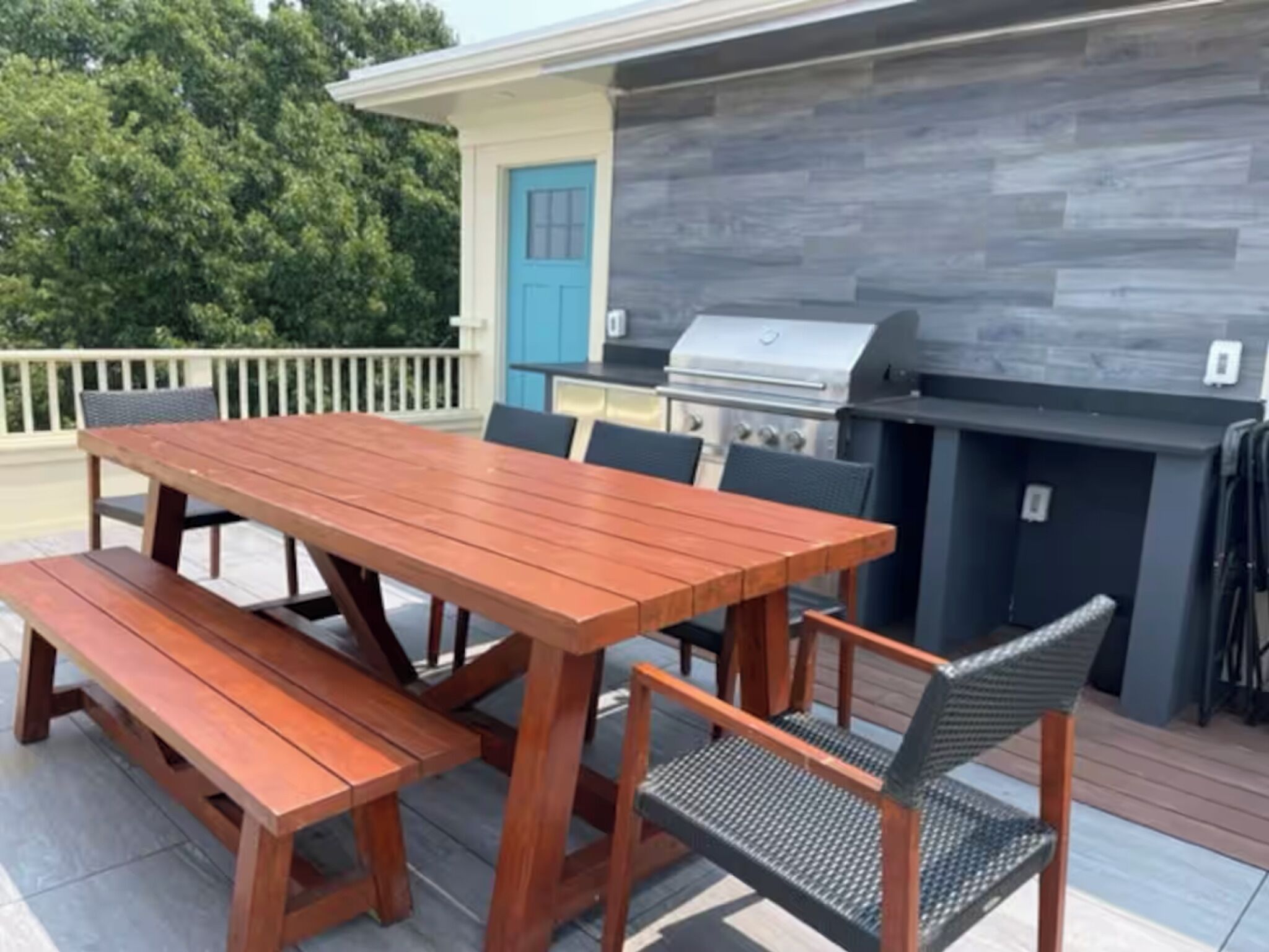 Un patio al aire libre con mesa y bancos de madera, una parrilla y una puerta azul.