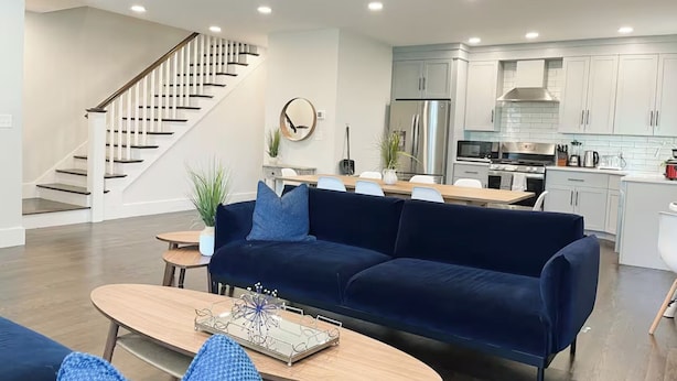 A modern living room with a dark blue sofa, wooden coffee table, and a staircase leading to an upper level. - 6-bed, Close to City, Roof deck! Private Bathroom per Bedroom! (Boston)