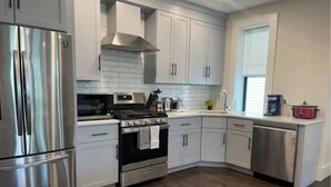 A modern kitchen with stainless steel appliances, white cabinetry, and a wooden floor. - 6-bed, Close to City, Roof deck! Private Bathroom per Bedroom! (Boston)