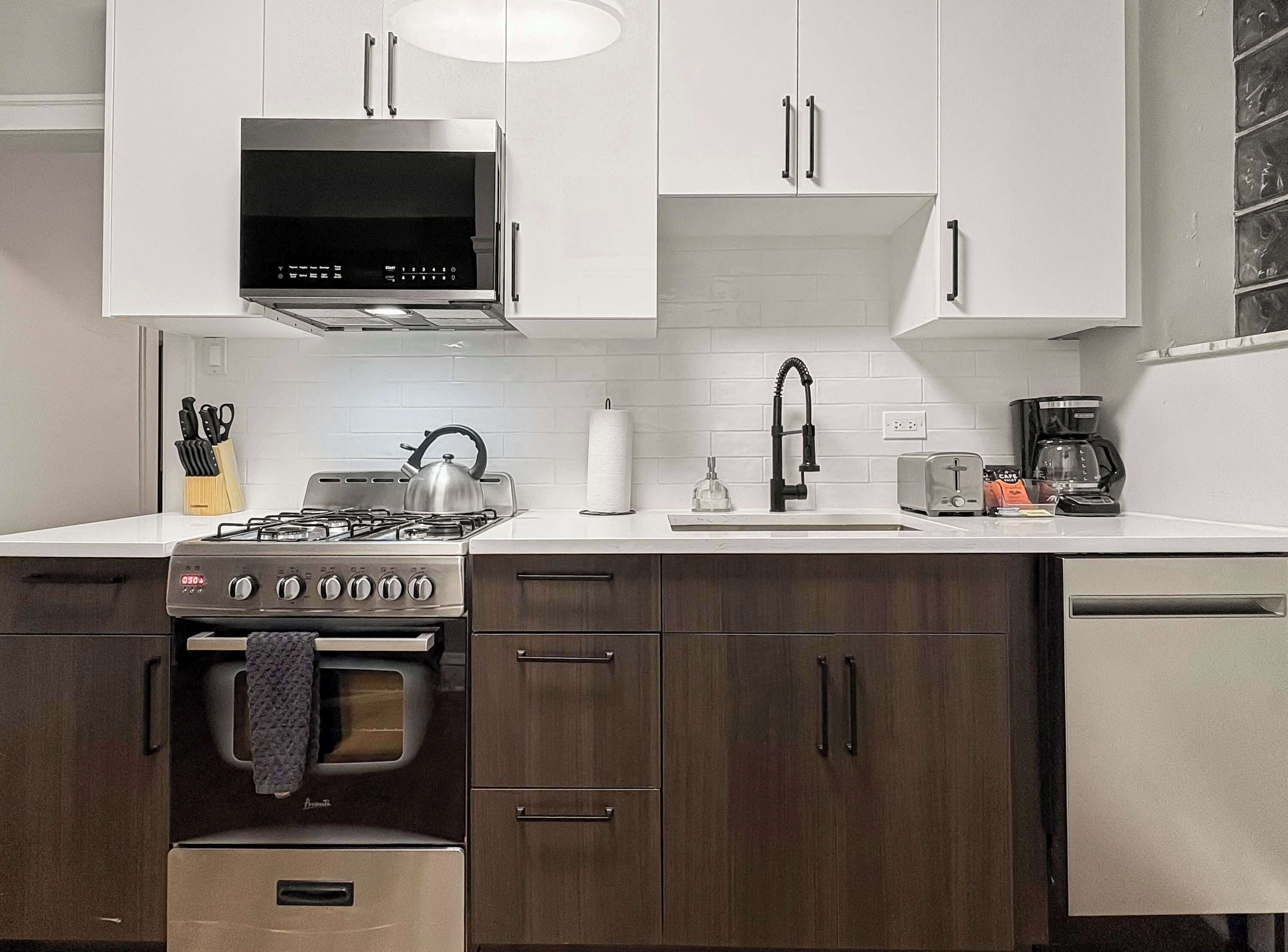 A modern kitchen with white cabinets, a stainless steel range, a kettle, a coffee maker, and a toaster.