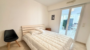 Un dormitorio con cama, una silla, una mesita y vistas al exterior.