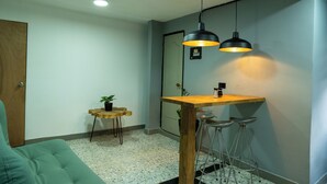 A small, modern room with a wooden table and two bar stools, a green sofa, and a small plant on a wooden stool. - Exceptional Marinilla Apartment (Marinilla)