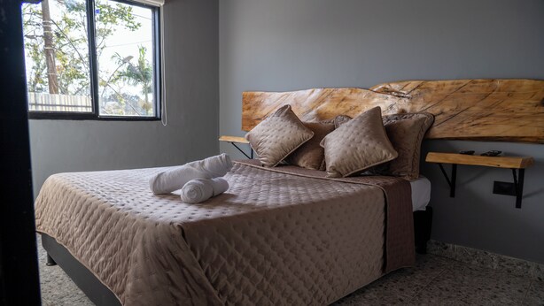 A neatly made bed with a quilted cover, a wooden headboard, and several pillows. - Exceptional Marinilla Apartment (Marinilla)