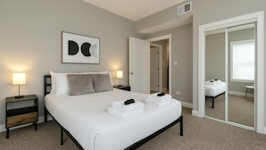 A bedroom with a bed, bedside tables, a mirror, and a door leading to another room.