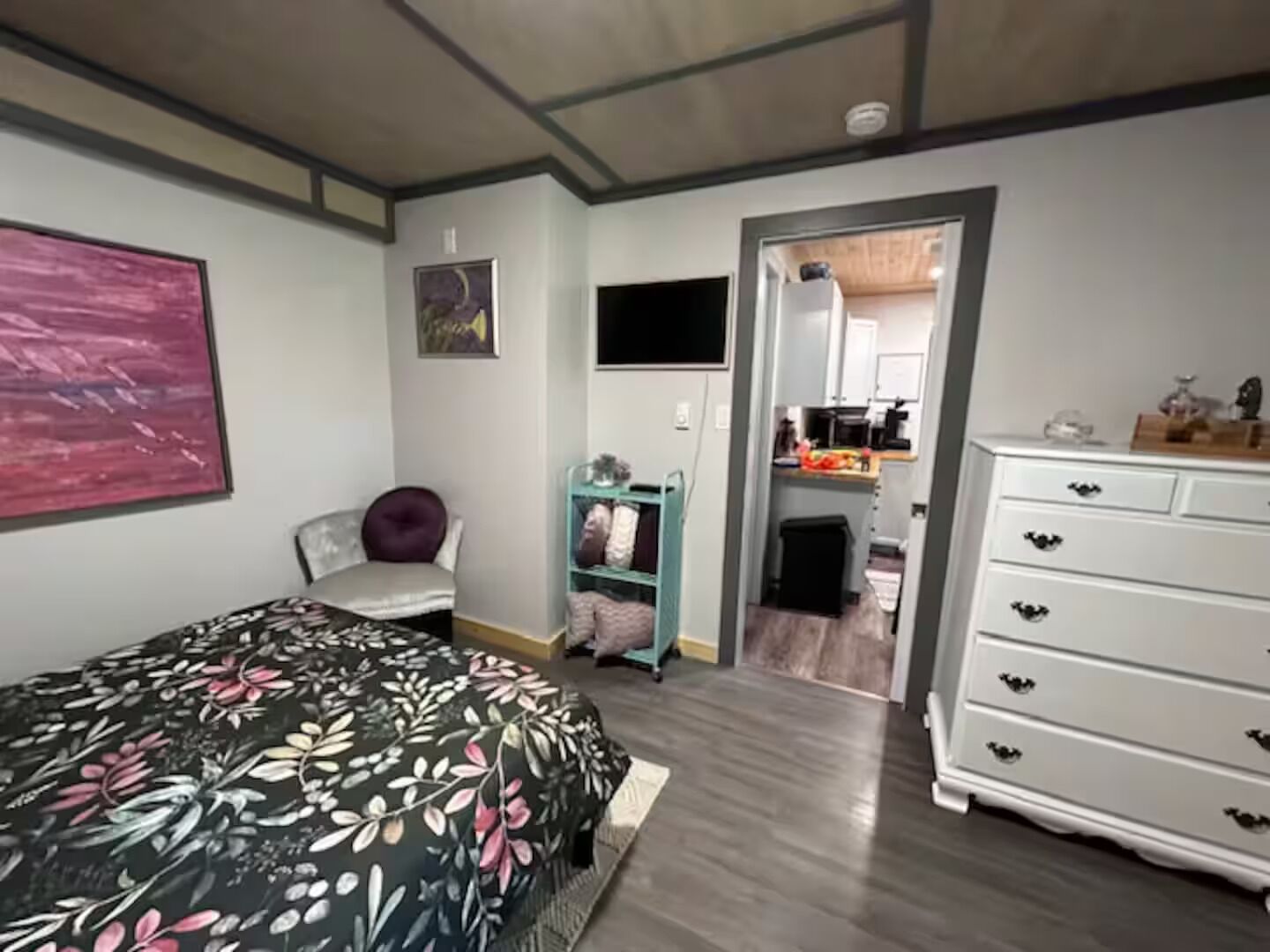 Een slaapkamer met een bed, een kaptafel, een stoel, een plank en een schilderij aan de muur.