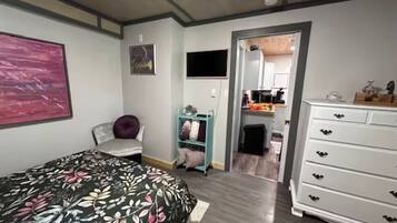 Een slaapkamer met een bed, een kaptafel, een stoel, een plank en een schilderij aan de muur.