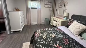 A bedroom with a bed, dresser, vanity, and a window with curtains.
