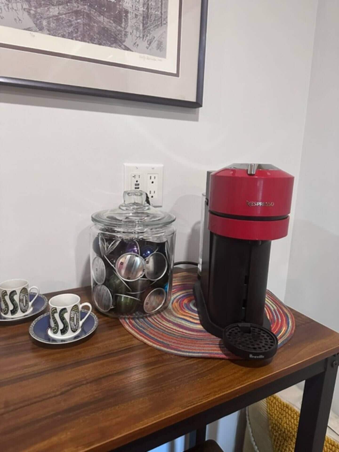 A coffee maker on a table with a glass jar of coins and two mugs with 'SSO' text.