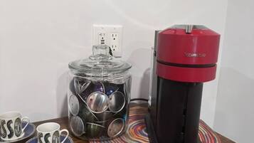 A coffee maker on a table with a glass jar of coins and two mugs with 'SSO' text.