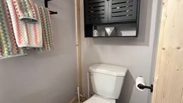 Un baño pequeño con inodoro, un cubo de basura y un perchero con toallas de colores.