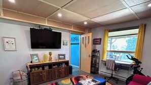 A living room with a colorful rug, a blue bench, a pink sofa, a TV mounted on the wall, and a window with curtains.