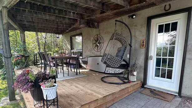 A covered patio area with a wooden deck, outdoor seating, and a hanging chair.