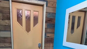 A wooden door with a glass panel, a bench, and a blue wall with a mirror.