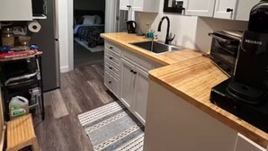 A compact kitchen with white cabinets, a wooden countertop, a coffee maker, and a small rug.