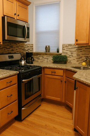 A kitchen with wooden cabinets, a stainless steel stove, a microwave, and a window with blinds. - 2BR on N Halsted St: Lakeview Living (Chicago)