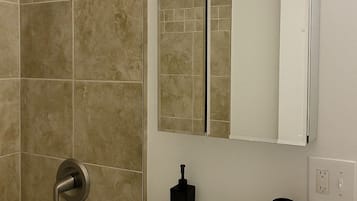 Ein Badezimmer mit einem weißen Waschbecken, einem Spiegel, einer Dusche und einer Lampenleuchte.
