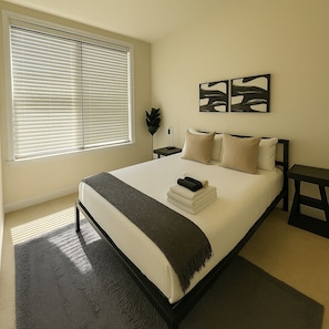 A bedroom with a large bed, a bedside table, a nightstand, a window with blinds, and a wall-mounted artwork. - Comfortable 3BR/2BA Haven | Ideal for Families (Chicago)