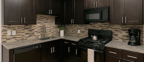 Una cocina moderna con muebles oscuros, un microondas, una estufa y una cafetera.