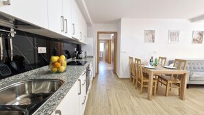 A modern kitchen with granite countertops, a stainless steel sink, and a fruit bowl. There is a dining area with a wooden table and chairs, and a grey sofa. - A QUIET PLACE 5 MINUTES WALK FROM THE CENTER OF MONDARIZ. (Mondariz)