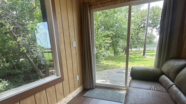 Une pièce avec un plancher en bois, un canapé en cuir marron et une grande fenêtre avec des rideaux.
