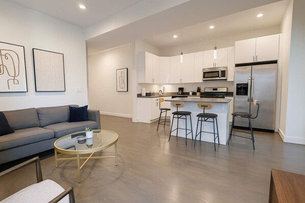 A modern kitchen with white cabinets, stainless steel appliances, and a bar area with stools.