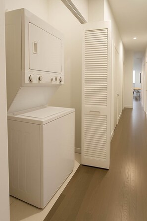 A laundry room with a front-loading washer and dryer, a white door with a vent, and a wooden floor.