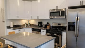 Una cocina moderna con armarios blancos, electrodomésticos de acero inoxidable, una isla central e iluminación colgante.