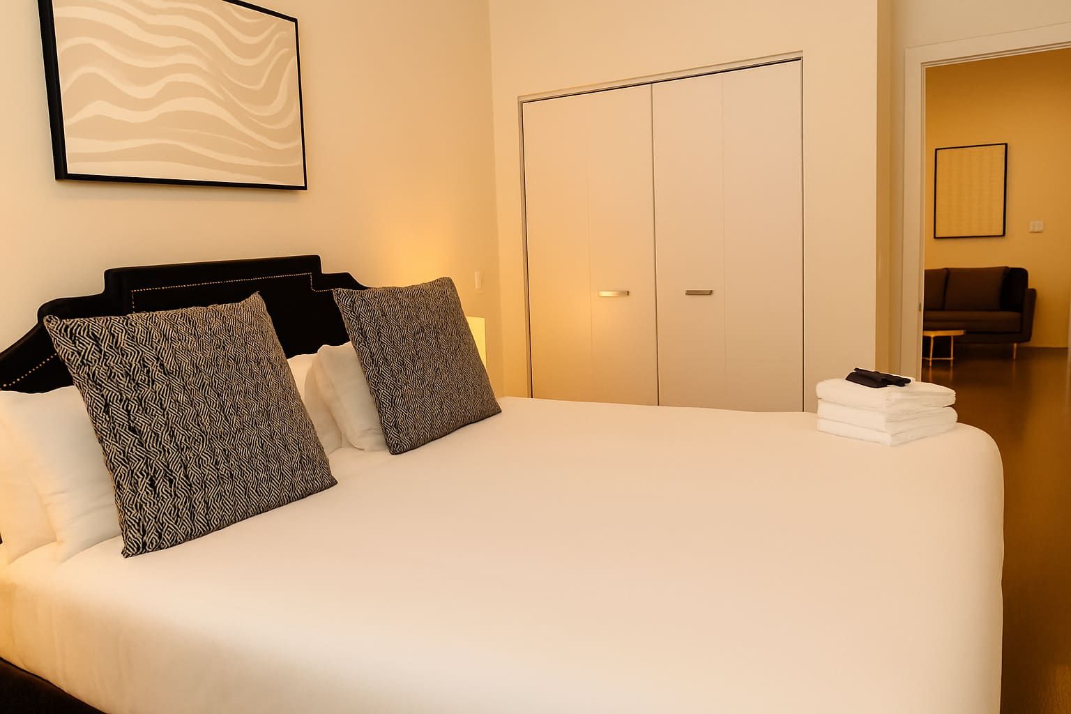 A hotel room with a large bed, a wardrobe, and a framed artwork on the wall.