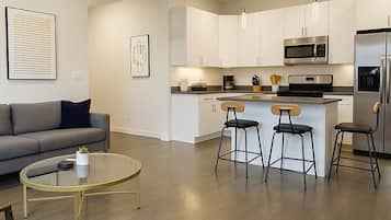 Una cocina moderna con armarios blancos, una isla central con taburetes, un microondas y un refrigerador.