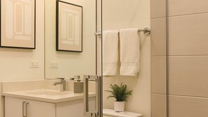 Ein modernes Badezimmer mit Duschkabine aus Glas, einer weißen Toilette, einem Waschbecken mit Spiegel und einer Topfpflanze.