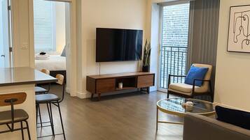 Una sala de estar moderna con una televisión de pantalla plana, un sofá, una mesa de centro y una zona de comedor con un taburete de bar.