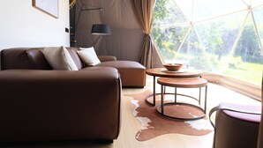 A modern living room with a brown sofa, a round coffee table, and a view through large windows.