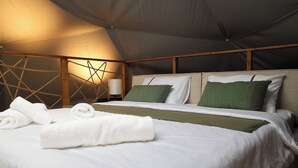 A tent-style room with a bed, white linens, green pillows, and a lamp.