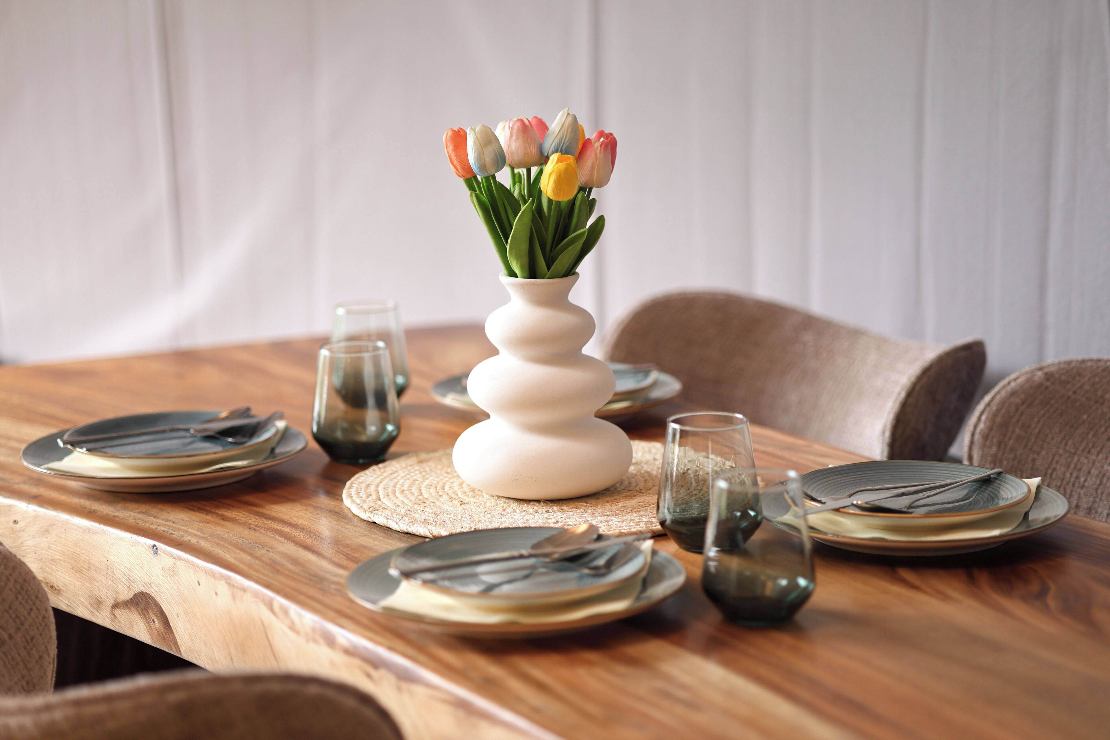Een houten eettafel gedekt met borden, bestek en een vaas tulpen.