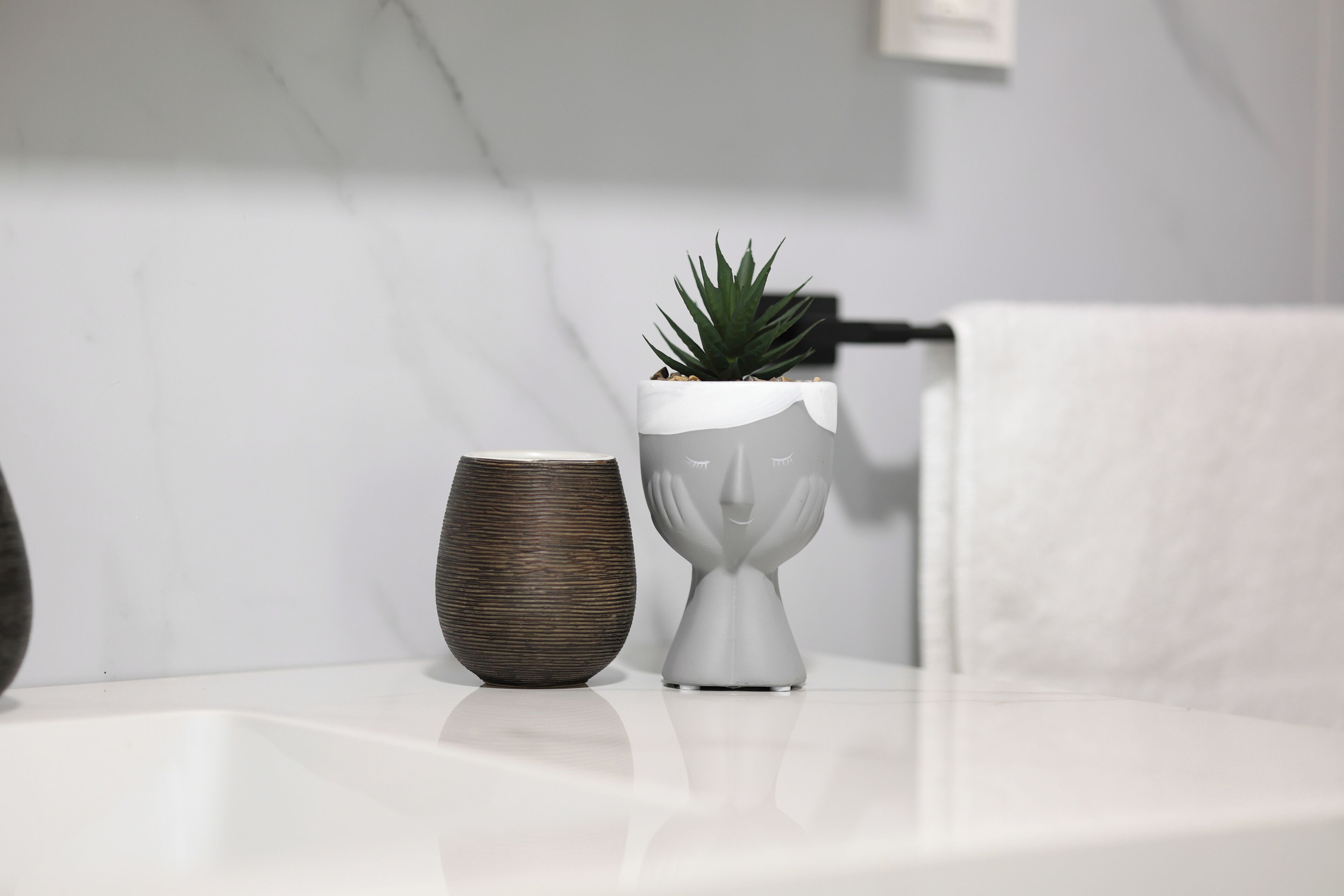 Un baño con encimera de mármol blanco, una planta en maceta y un florero decorativo.