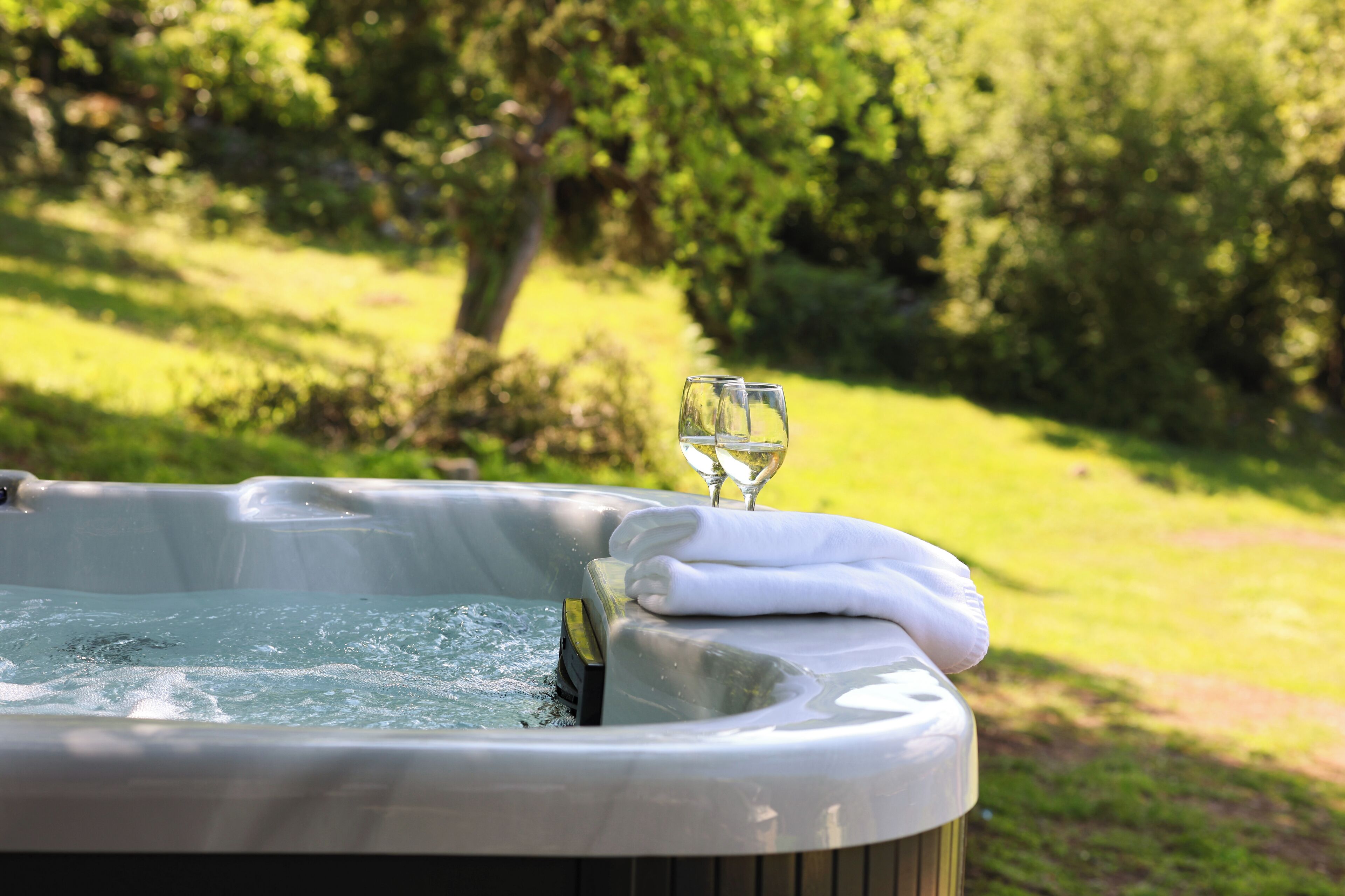 Ein Whirlpool mit Handtuch und zwei Weingläsern, eingebettet in einen üppigen Garten.