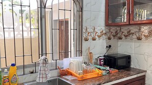 Una cocina con salpicadero de mármol, ventana con rejas de metal, armarios de madera y encimera con diversos utensilios de cocina.