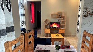 Una sala de estar con chimenea, un sofá, una mesa de centro y una mesa de comedor con manteles florales.