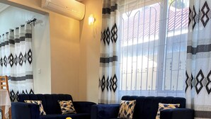 Una sala de estar con dos sofás azul oscuro, una mesa de centro de madera, alfombras con diseños y cortinas decorativas.