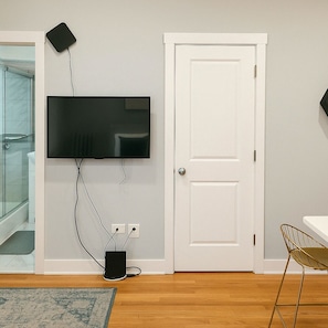 A room with a mounted flat-screen TV, a white door, and a small table with a chair.