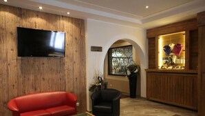 Ein Wohnzimmer mit einem roten Sofa, einem schwarzen Sessel, einem Glastisch und einem flachbildfernseher, der an einer Holzwand angebracht ist.