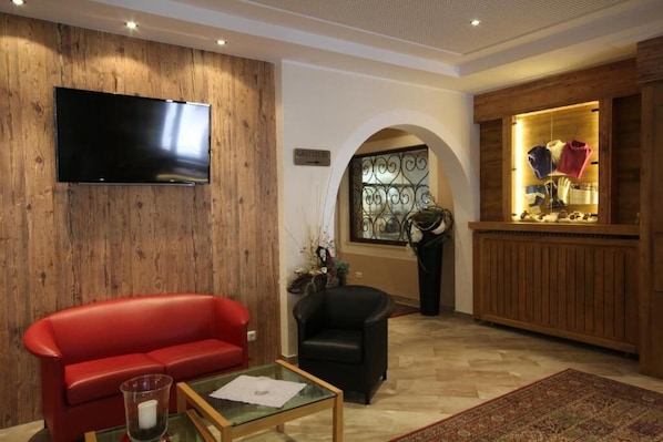 Una sala de estar con un sofá rojo, un sillón negro, una mesa de centro de vidrio y un televisor de pantalla plana montado en una pared de madera.