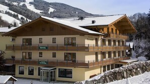 Ein Hotel mit Holzfassade, mehreren Balkonen und Blick auf schneebedeckte Berge.