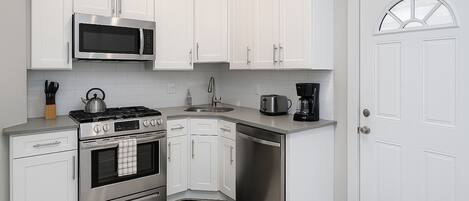 A modern kitchen with white cabinetry, stainless steel appliances, and a black rug.