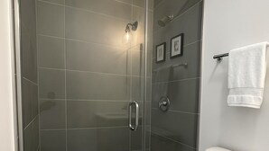 Et moderne badeværelse med en bruseniche med glasvægge, et hvidt toilet og en håndklædestang.