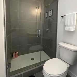 Une salle de bain moderne avec une douche à parois de verre, des toilettes blanches et un porte-serviettes.