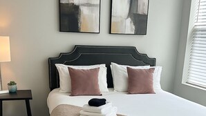 Et soveværelse med en stor seng, et natbord, en lampe og abstrakt kunst på væggen.