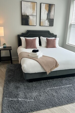 Une chambre avec un grand lit, une table de chevet, une lampe et des œuvres d’art abstraites accrochées au mur.