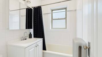 Une salle de bain avec un lavabo blanc, un miroir, une baignoire et une fenêtre.